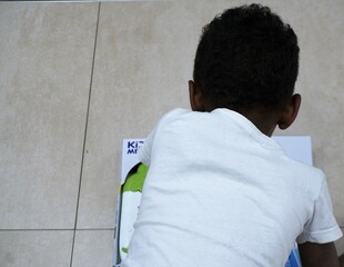 Afrikanischer kleiner Junge mit weißem T-Shirt vor Spielzeug am weißem Boden in Geschäft 