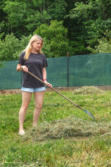 Girl collects dry grass with garden rake