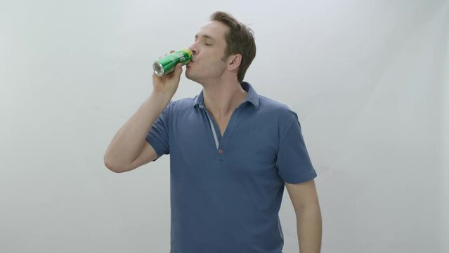 Young man drinks fizzy Sprite beverage from metal bottle. Slow motion video. The young man is drinking Sprite and is happy to cool off. Slow motion video. Indoor studio isolated on white background.
