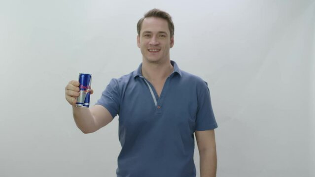Young man drinks fizzy RedBull beverage from metal bottle. Slow motion video. The young man drinks RedBull and is happy to cool off. Slow motion video. Indoor studio isolated on white background.