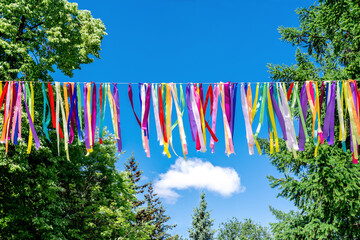 Hanging colorful ribbons on the background of trees and blue sky. Decorative decoration of the holiday outside the city