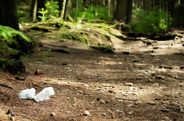 Full doggy bag left on trail. White dog poop bag at the edge of a hiking trail of defocused...