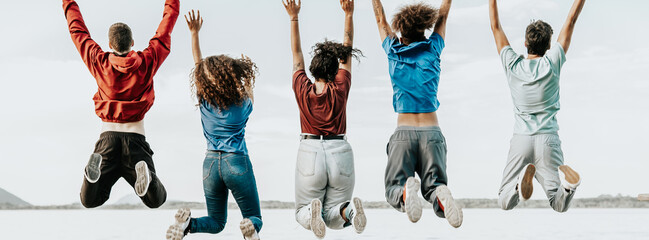 group of cheerful young multiracial friends jump over white background - obrazy, fototapety, plakaty