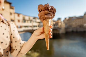 Holding chocolate ice cream in a waffle cone on background of the Old bridge in Florence, Italy....