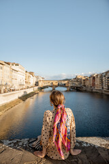 Young woman enjoys beautiful view on famous Old bridge in Florence, sitting back on the riverside...