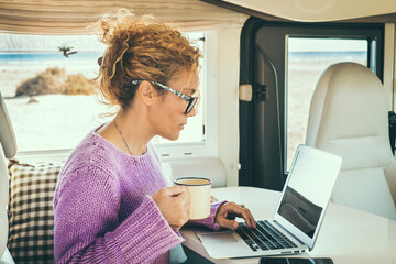 Adult woman use laptop sitting inside a camper van. Concept of digital nomad lifestyle and wireless...
