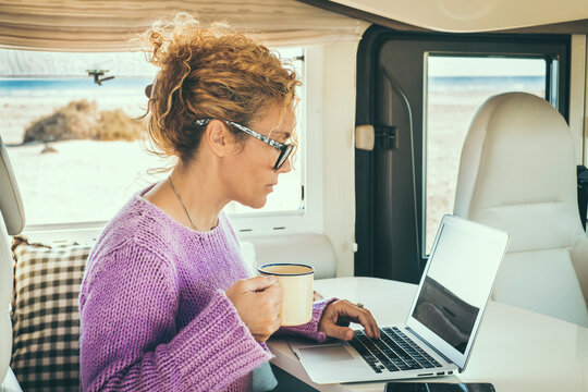 Adult woman use laptop sitting inside a camper van. Concept of digital nomad lifestyle and wireless internet connection during travel. Van life and smart working job concept. Cute female write on pc