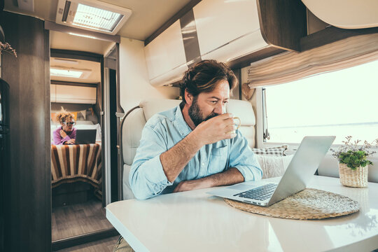 Couple use computer inside camper van during travel vacation or van life lifestyle. Modern man and woman work together on laptop in alternative office motor home. Digital nomad and smart free working