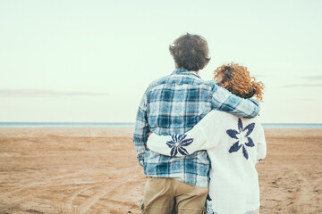 Rear view portrait of couple in love admiring the beach and ocean hugging with love. Romantic life in winter holiday vacation. People in relationship embracing. Love and togetherness concept - Powered by Adobe