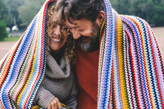 Overjoyed adult caucasian couple under a colorful cover laugh and have fun together with love and friendship. Young mature people in outdoor leisure romantic activity. Man and woman laughing a lot
