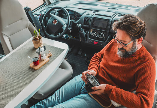 Adult man sitting inside motor home camper van cabin using photo camera and drinking coffee. Concept of travel and adventure lifestyle with vehicle. Alternative life for mature people. Van life