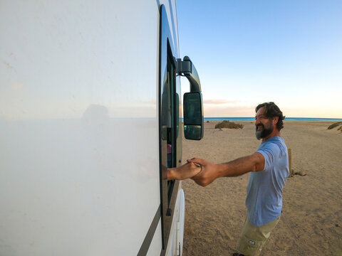 Outside view of couple holding hands. Woman inside a camper van and man outside smiling. Travel for holiday vacation lifestyle concept. beach and ocean in background