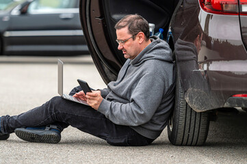 man sitting on asphalt by car and working on laptop, working remotely, traveling