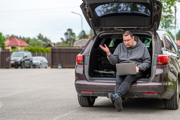 Fototapeta na wymiar a man sitting in the open trunk of a car and working with a laptop, mobile technology, remote work