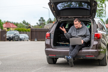 a man sitting in the open trunk of a car and working with a laptop, mobile technology, remote work