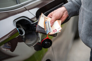 hand of man that puts money into the tank of car, close up, concept of expensive fuel, fuel crisis