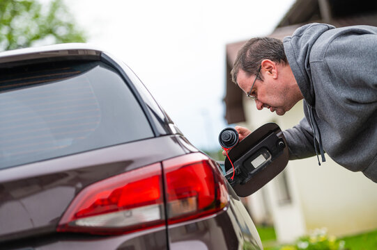 Worried Man Looking At Open Car Fuel Tank, Concept Of Rising Fuel Prices