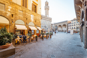 Beautiful street with cafe terrace near central square in Florence city, Italy. Vecchio palace with tower on the background. Traveling italian landmarks concept