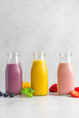 Colorful summer fruit and berry smoothie drinks in bottles on white background. Healthy refreshing drinks