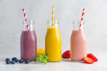 Colorful summer fruit and berry smoothie drinks or milkshake in bottles with straw on white...