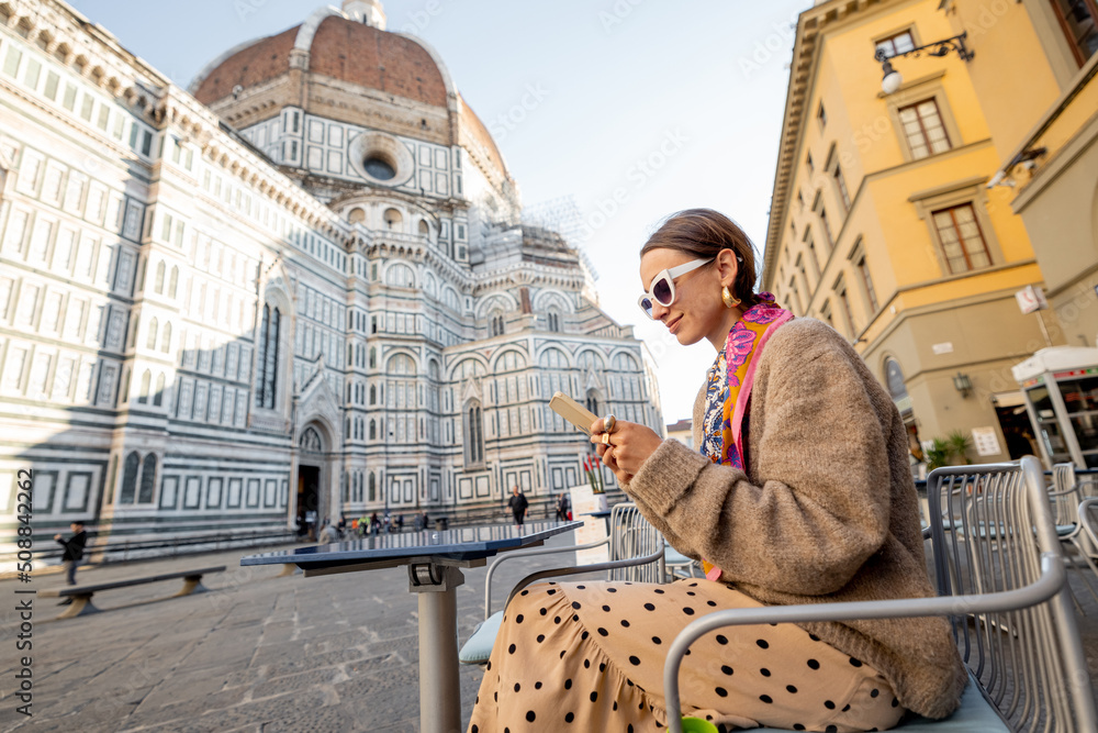 Wall mural stylish woman sitting with phone on cafe terrace near famous duomo cathedral in florence during morn