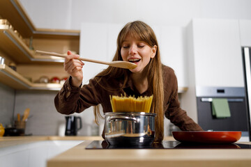 Young woman is tasting food while cooking in kitchen at home