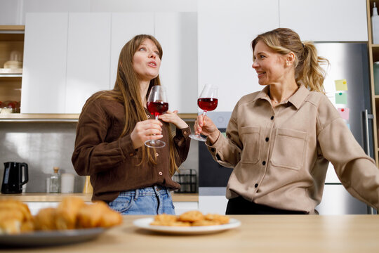 Mother And Adult Daughter Gossiping And Drinking Wine In The Kitchen