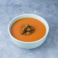Tomato cream soup with vegan jerky in blue bowl on concrete surface