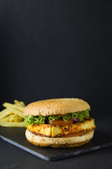 Tofu burger with veggie bun, lettuce, tomato slices and french fries on the black slate plate shot in low key with copy space