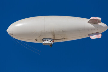 Fototapeta na wymiar A white blimp without any markings, a blank canvas or banner space with a blue sky in the background. A lighter than air ship flying high with room to put your own ad.