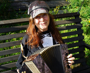 Elderly woman with  red hair and a cap sits outside and plays a diatonic button accordion
