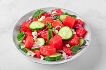 Summer fruit and vegetable salad made of watermelon, cucumber, soft cheese and onion on white table