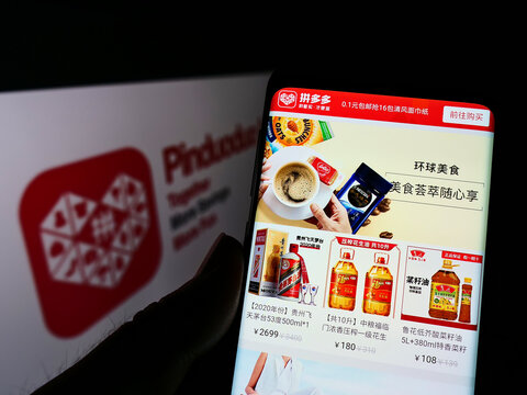 Stuttgart, Germany - 05-22-2022: Person holding smartphone with webpage of Chinese e-commerce company Pinduoduo Inc. on screen in front of logo. Focus on center of phone display.
