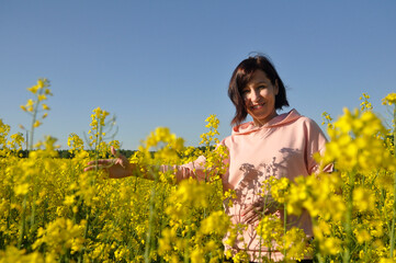 Naklejka na ściany i meble Beautiful young woman in the middle of a field of yellow rapeseed or canola flowers.