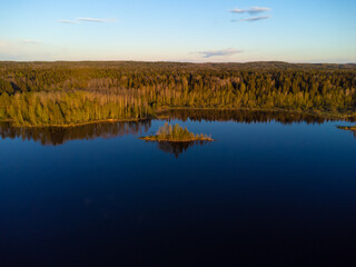 River bank covered with forest in the rays of the setting sun. Small island off the coast
