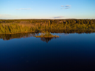 River bank covered with forest in the rays of the setting sun. Small island off the coast