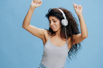 MOVING TO MUSIC. Overjoyed dancing beautiful Latin female with afro touch headphones, listen music. Good offer for Phone pc fashion brands, music platform ad. Studio PORTRAIT isolated blue background