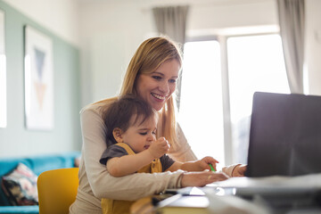 Mother working on laptop with child sitting on her lap 
