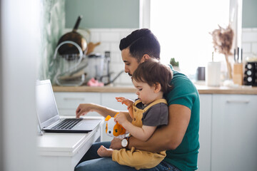 Dad working on laptop with child sitting on his lap 
 - obrazy, fototapety, plakaty