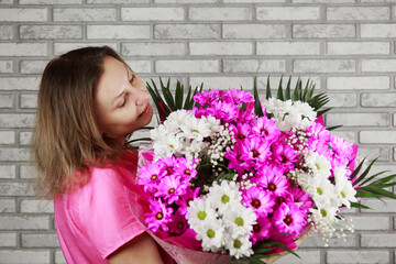 smiling blond woman holds great bouquet of pink chrysanthemum hydrangea and roses wrapped in paper.