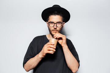 Studio portrait of young guy drinking cold tea with straw from paper cup.