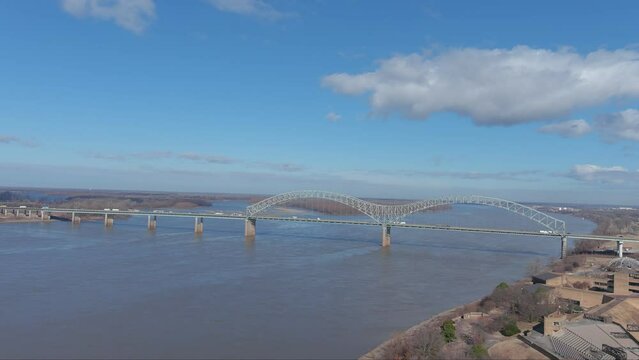 aerial footage of the Hernando de Soto Bridge over the vast flowing waters of the Mississippi river with cars and trucks driving across the bridge and blue sky with clouds in Memphis Tennessee USA