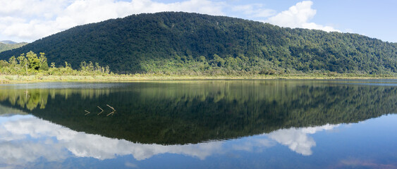 Stunning reflection of bush-clad mountains in calm surface of Lake Moeraki