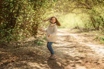 Naklejka na ściany i meble Little pretty girl on walk in sunny spring park. Fairy forest. Child with long hair listens to music, sings, smiles and rejoices. High quality photo