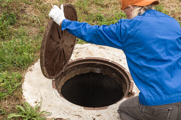 A working plumber opens a sewer hatch. Maintenance of septic tanks and water wells