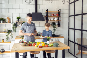 Handsome father and his teenager son spending quality time together. Men doing chores, cooking healthy vegetable salad, tasty food in the kitchen at home