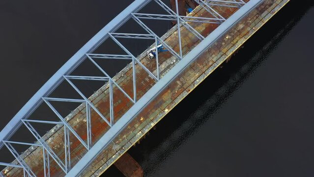 4k aerial footage. Unfinished big bridge across the river, under it rusty barges. Construction work on the bridge. Metal constructions. Construction crane works. Overall industrial structures