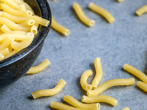 Closeup of Italian food yellow raw uncooked vermicelli, macaroni, noodle, pastry, pasta on the isolated bowl (close-up,meal, cuisine, cooking, gray, dry, dish, studio, plate, dinner, tile, cement)
