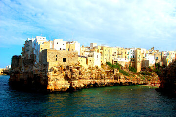 Lovely panorama of the Adriatic sea and a rocky coast of Polignano a Mare with some houses as well as the beach at Lama Monachile on the right under the blue sky covered with light clouds