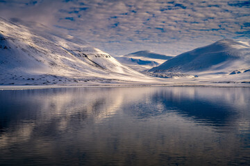 2022-05-15  SNOW COVERED ROUNDED MOUNTAINS WITH A BEAUTIFUL REFLECTION IN THE OCEAN AND A CLOUDY SKY IN THE ARCTIC NEAR SVALBARD NORWAY